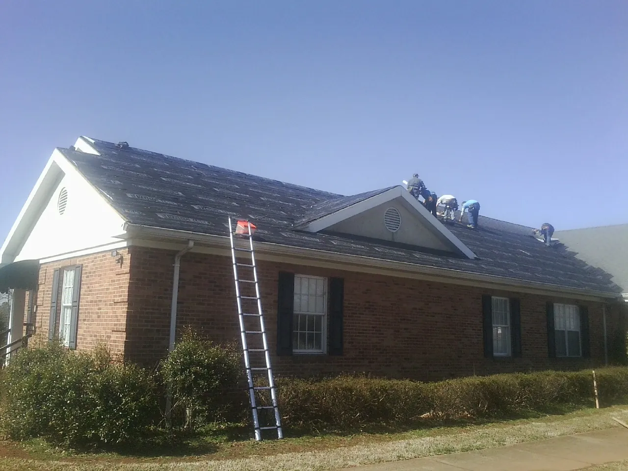 Crew tearing shingles off a brick ranch roof with a ladder set — Metal Roof Repair work by our crew in Mc Cutchenville