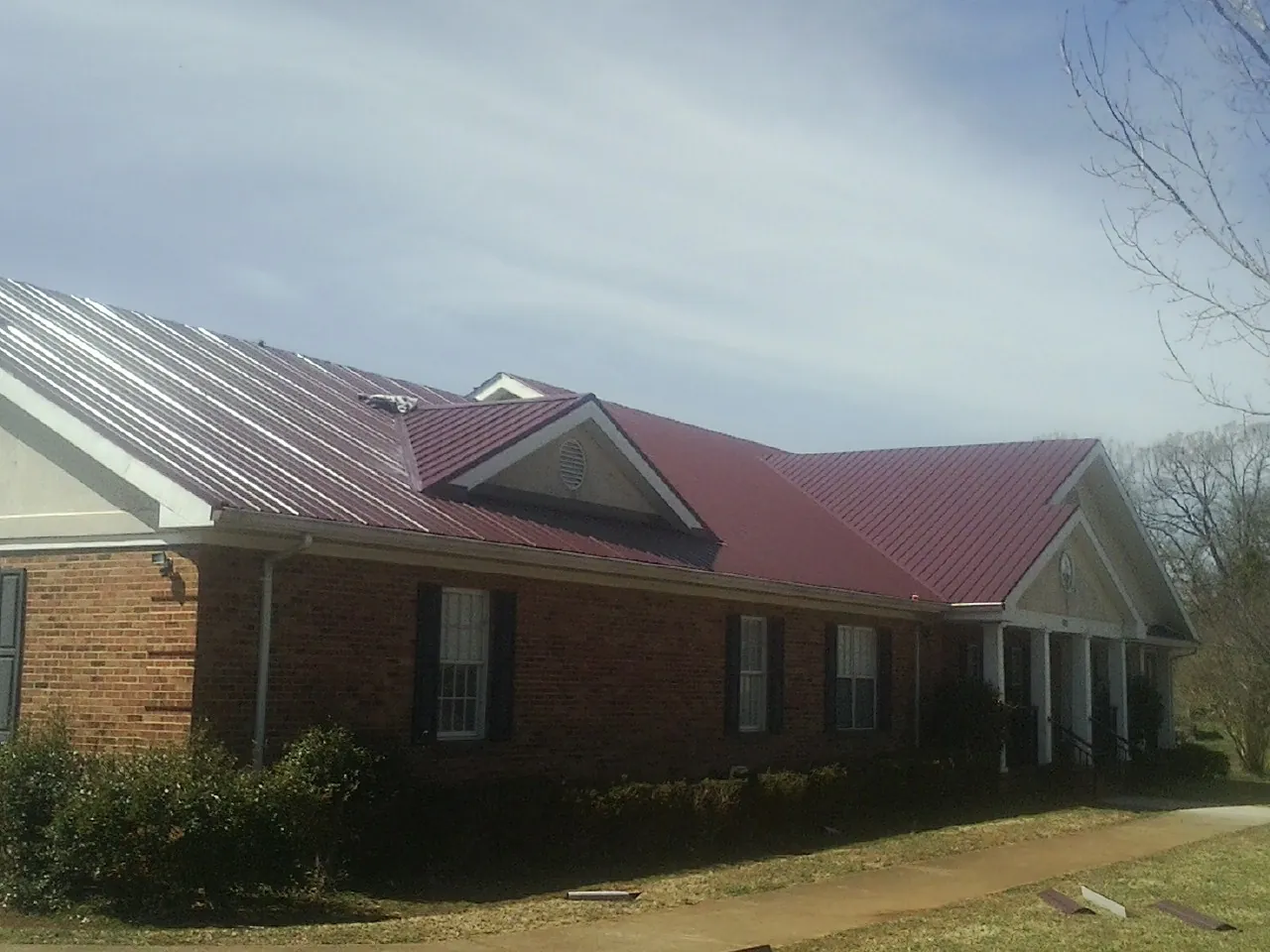 Red metal roof with gabled entries on a long brick building, from a Hail Damage Roof Repair job in Mc Cutchenville
