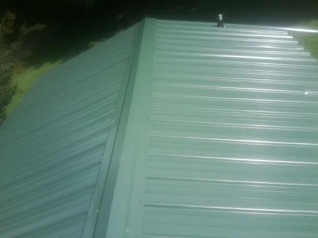 New green metal panels meeting at the ridge of a roof — Flat Roof Repair work by our crew in Mc Cutchenville