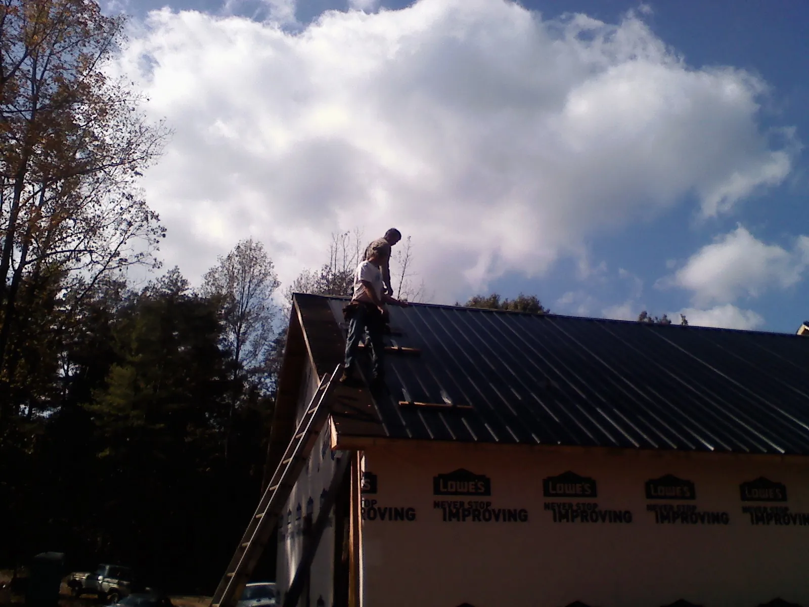 Roofer fastening dark metal panels high against a cloudy sky, from a Roof Inspection job in Mc Cutchenville