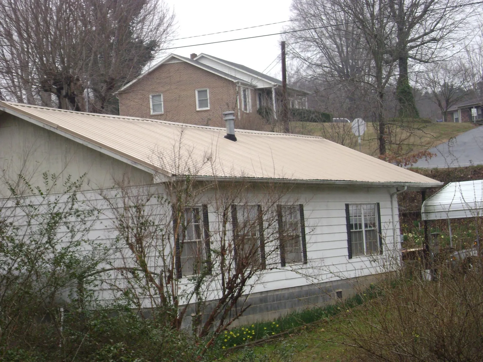 Tan metal roof on a white sided house set into a hillside — Commercial Roofing by Roofing Brothers in Mc Cutchenville